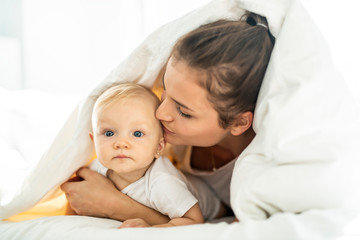 Portrait of young mother with infant baby girl liying on the bed covered with a white blanket