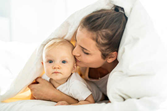 Portrait of young mother with infant baby girl liying on the bed covered with a white blanket