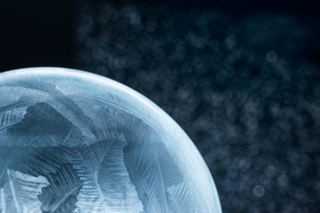 Naklejka na ściany i meble Frozen snow globe christmas magic ball with flying snowflakes. Winter Background. For Christmas and New Year Holidays precious backdrop. Ice patterns frosted on ball of soap against blue shiny