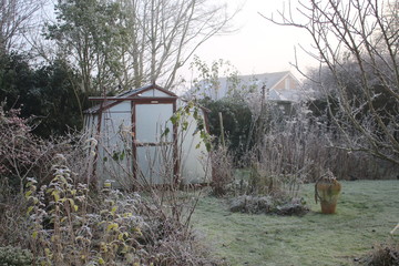 Landscape of frozen Winter garden in heavy white frost with misty pane glass greenhouse, icy lawn...