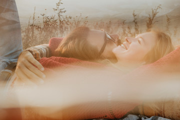Couple in sweaters  chilling and hugging on blanket outdoors in sunrise