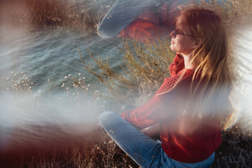 Rebel careless ginger girl in red sweater smoking near sea in sunrise