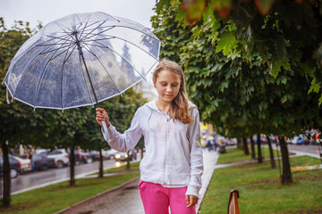 School gir under an umbrella walking in the rain in the city alley.