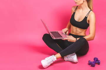 Happy beautiful fitness woman using laptop over pink background.