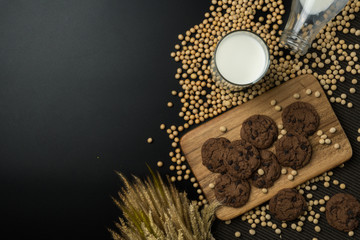 Obraz na płótnie Canvas top view of the chocolate chip cookies on the wooden tray, a glass of soy milk, a pile of soybeans, a bottle of soy milk with dried wheat bouquet and the napery.