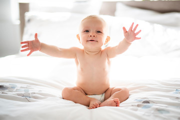 Cute baby girl sit on white sheet at home