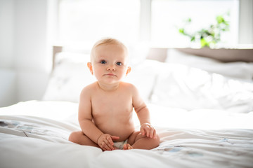 Cute baby girl sit on white sheet at home
