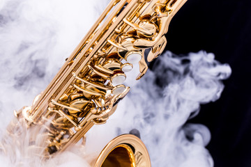 A gold plated saxophone in smoke on a black background