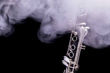 A black clarinet with silver plated keys in smoke on a black background