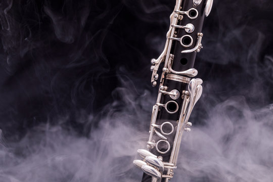 A black clarinet with silver plated keys in smoke on a black background