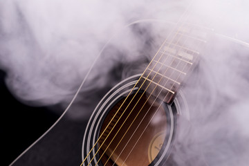 A part of a black classical guitar in smoke on a black background