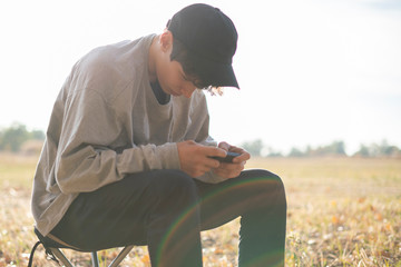 young person sitting in the middle of gorgeous amazing summer field and using smarphone f