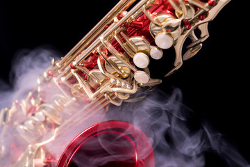 A red lacquered saxophone with gold plated keys in smoke on a black background