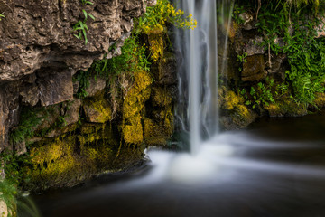 A small waterfall falling over rocks with moss and grass