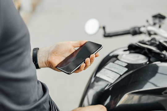 Close up of biker holding mobile phone while sitting on motorcycle.