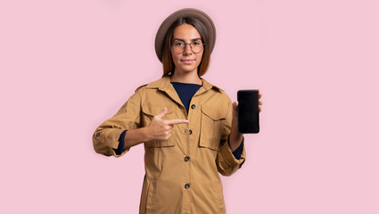 Brunette woman pointing to black smartphone screen, isolated over pink background