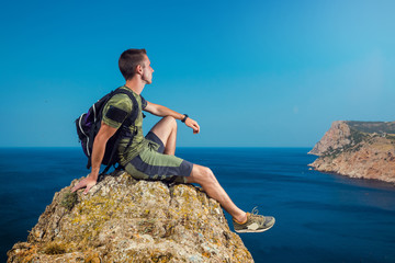 Man hikers sitting on a rock and looking at sea and mountain landscape. The athlete relaxes on a stone and enjoying the view from the cliff.
