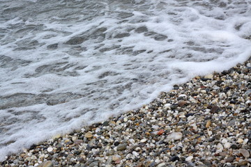 A foamy sea wave running to a pebbled beach