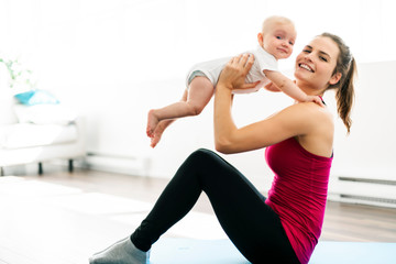 A Portrait of beautiful young mother in sports wear with her charming little baby in training...