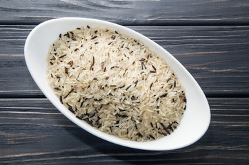 Top view, close up, macro. White oblong bowl filled with wild rice. Dark wooden background.