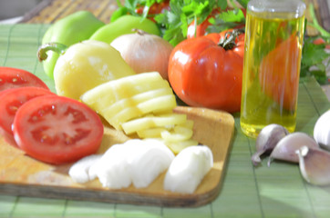 Chopped tomatoes on a board, onions, garlic, greens. Ingredients for cooking salad or soup. Healthy food diet. Photo on top of fresh vegetables, cutting board, oil, knife,