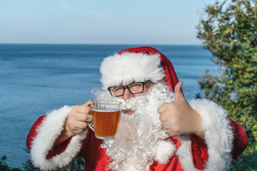 Fat man in glasses dressed as Santa drinking beer on the ocean. Funny, drunk and happy