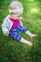 Baby girl sitting on the grass, sucking a pacifier.