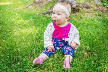 Baby girl sitting on the grass, sucking a pacifier.