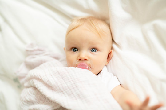 A cute baby with pacifier lying on a white bed