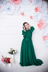 beautiful brunette woman in silk green dress posing with flowers on light background