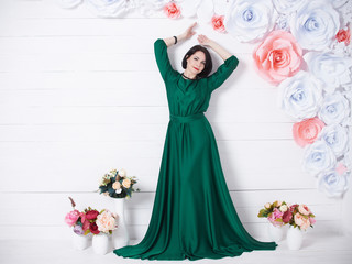 beautiful brunette woman in silk green dress posing with flowers on light background