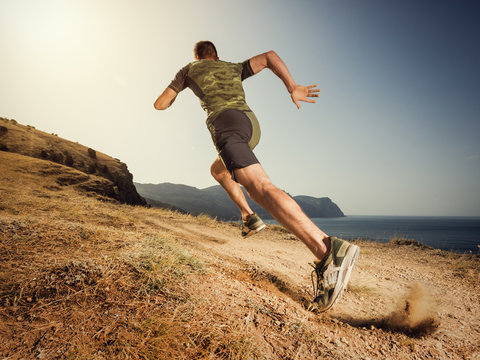 Young man runner running on a dusty country road. Jogger training workout in fitness shoe. Healthy lifestyle and sport concept.