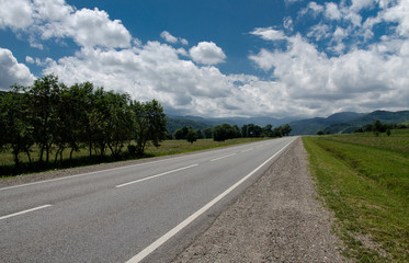 Empty asphalt road highway in the forested mountains, on the background a cloudy sky