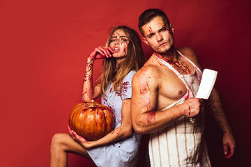 Zombie couple bare-chested man and vampire woman in blood and halloween makeup holding pumpkin. Isolated on red background. Models with bloody hands and blood on face.