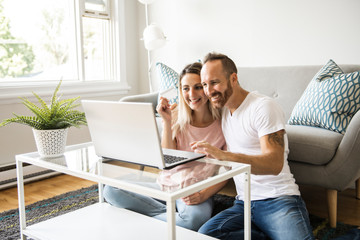 Excited young couple shopping online, holding credit card and looking at laptop at home