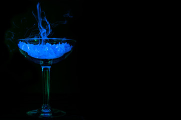Glowing blue drink with neon smoke in martini glass