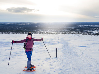 Pretty, young woman snowshoeing and enjoying splendid winter weather with abundance of snow