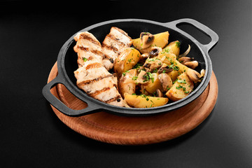 Close up of fried potatoes with mushroom chicken breast in frying pan on black background menu restaurant grill