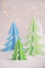 Origami 3D Xmas tree from paper on white background and bokeh lights. Merry Christmas and New Year card. Paper art style. Copy space. Selective focus