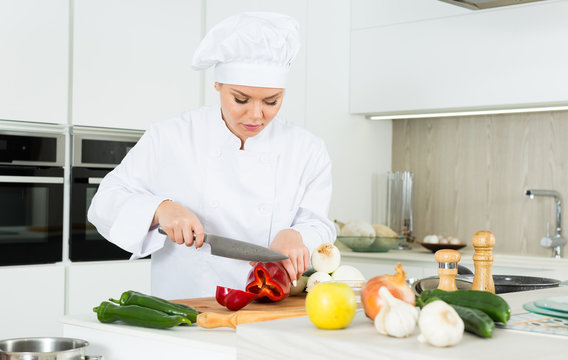Young woman cook preparing vegetables in white uniform