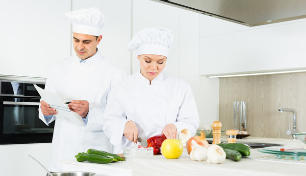 Chefs  in uniform  prepare vegetables with paper recipe on kitchen