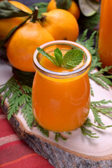 Orange smoothie topped with mint in glass jars surrounded by fruits