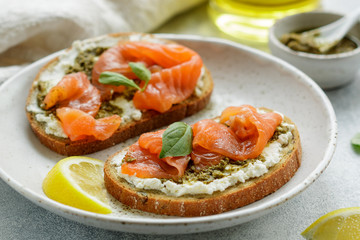 Bread toast with salted salmon, pesto sauce, lemon and cream cheese (ricotta). Gourmet snack. selective focus