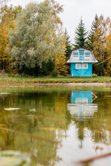 Fototapeta na wymiar Cute little colorful private real sauna house by the private lake shore in autumn, yellow autumn tree leaves.