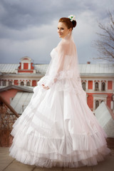 Fototapeta premium Portrait of a bride in a wedding dress and with a long veil on the background of the ancient city and a cloud in the autumn day.