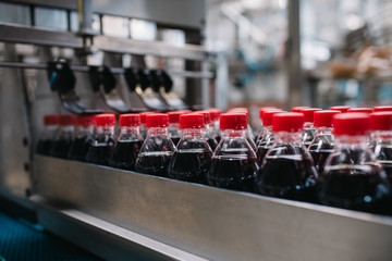 Bottling factory - Black juice or soft drink bottling line for processing and bottling juice into bottles. Selective focus.