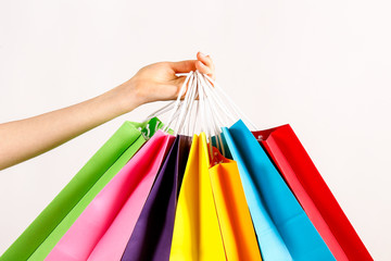 Cropped shot of female hand holding bunch of different colorful blank shopping bags over isolated white background. Many packets with in woman's arms. Black friday sale concept. Copy space, close up.