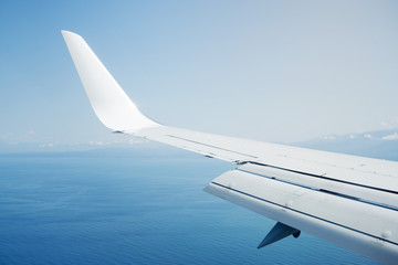 Fototapeta premium Wing of an airplane flying in the sky above the sea, view from the porthole