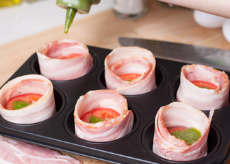 Cooking bacon egg muffins. Pouring pesto in cups from bacon with bread and tomato