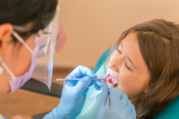 Cute little girl lying in a dentist chair and smiling at the camera while having an oral cavity...